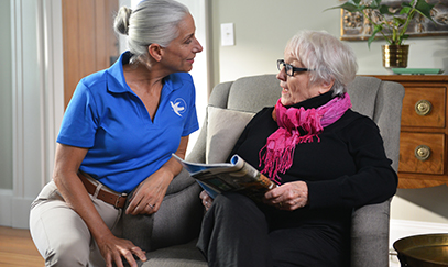 A Visiting Angels caregiver engaging with an elderly man with Alzheimer's, providing gentle support and encouragement in a warm home environment.