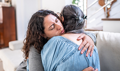 A Visiting Angels caregiver providing compassionate support to a family member at the bedside of an elderly patient in end-of-life care, highlighting empathy and comfort.